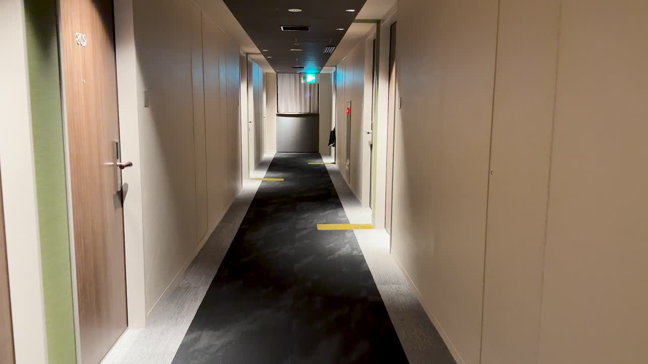 Una lenta carrellata in avanti attraverso un corridoio tranquillo e moderno di un hotel con illuminazione calda.