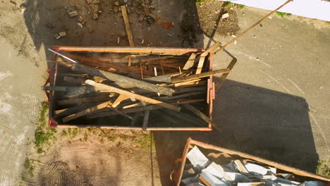 overhead view showing an excavator loading wooden debris into a dumpster during the cleanup of a demolition site