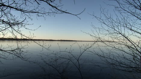 Trees-branches-framing-around-idyllic-lake-at-sunset