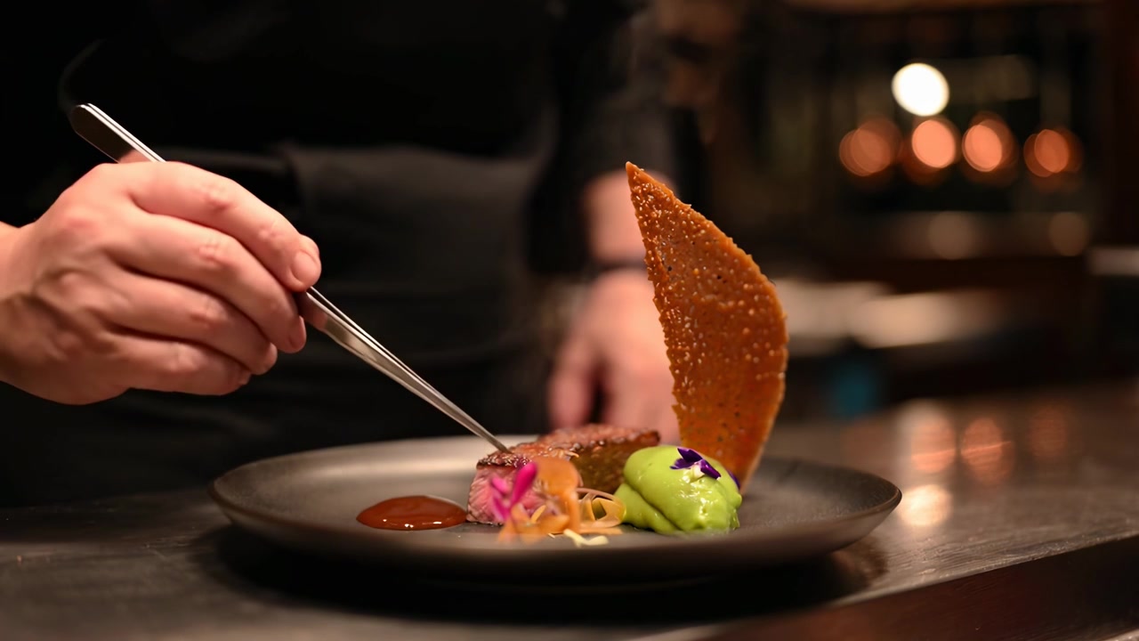 Kokk anretter en gourmet biffrett med presisjon på et restaurantkjøkken