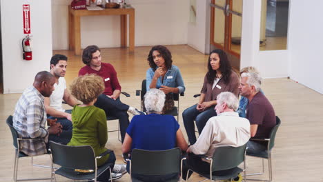 people sitting in circle attending self help therapy group meeting in community center