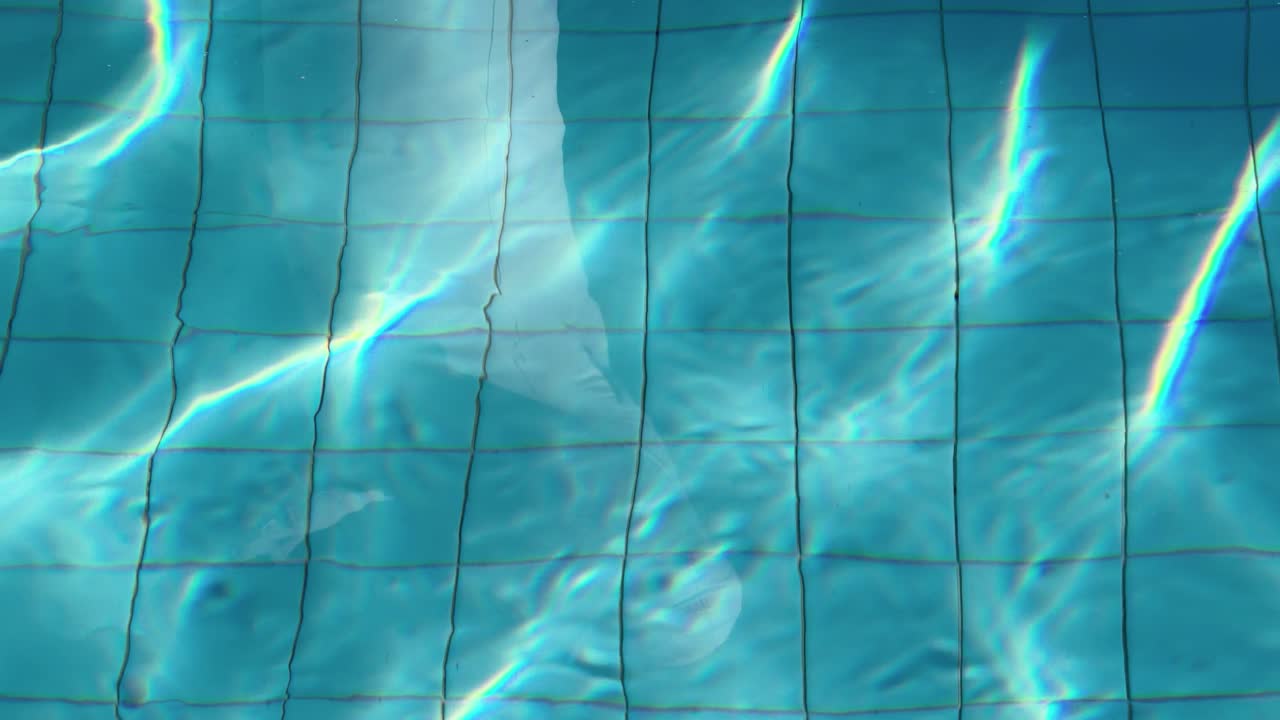 Sinar matahari yang cerah menciptakan pola kaustik pada air kolam yang berkeramik biru dengan bayangan manusia samar