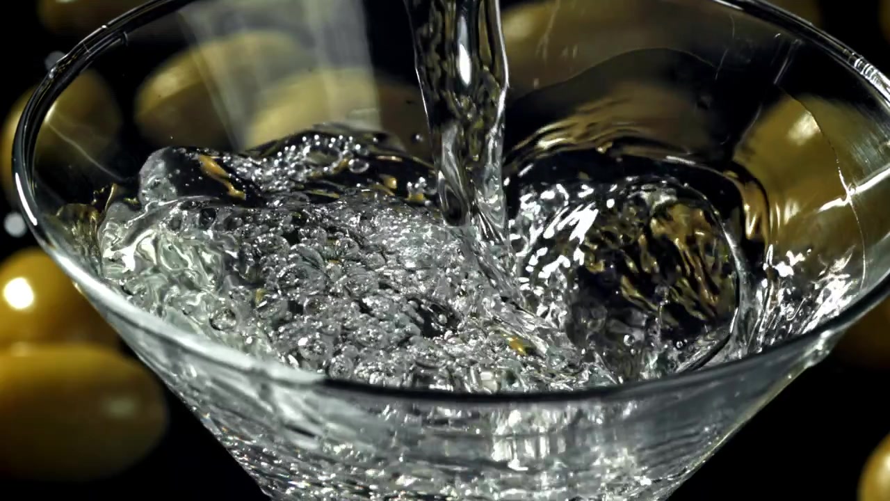 Liquido trasparente versato in un bicchiere da Martini con olive al rallentatore