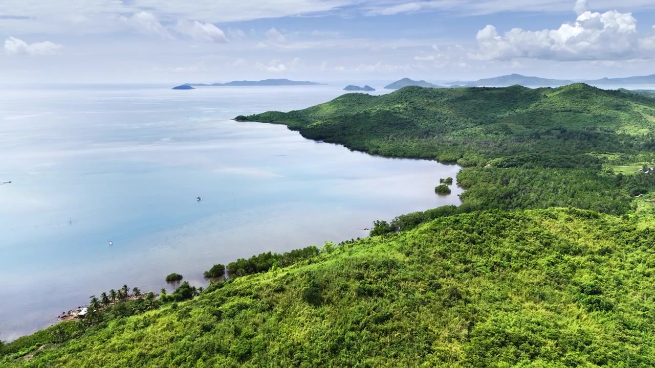 The drone glides past a hilltop overlooking the calm waters of the Sulu Sea, gently pushing forward over a lush mangrove shoreline. The scene reveals a tranquil tropical seascape