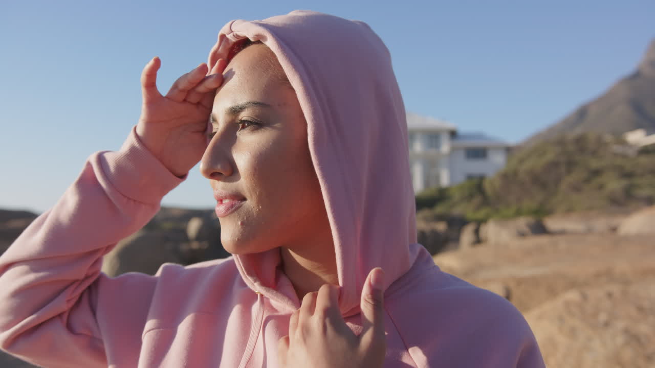 Donna asiatica con felpa rosa che si gode il paesaggio all'aperto, riparandosi gli occhi dal sole, con spazio per il testo.
