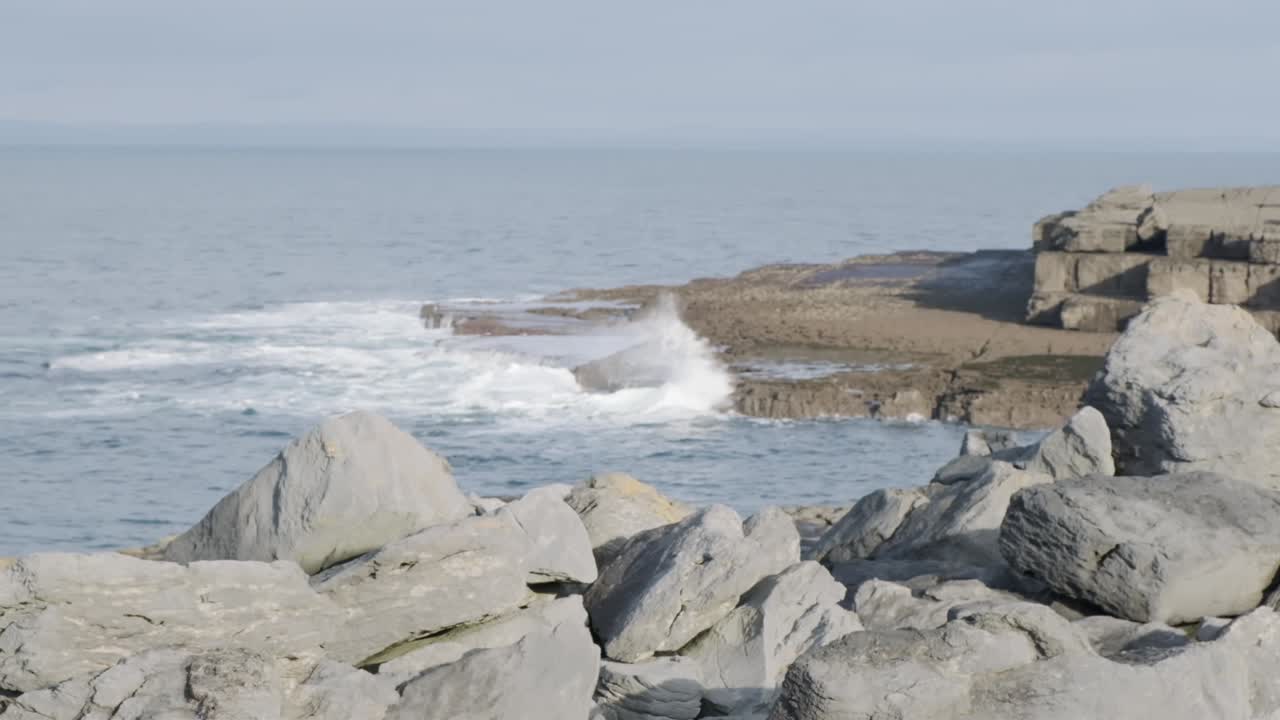 Rocky cliff in the foreground, waves crashing and splashing in slow motion in the background. Oceanic waves break on coastline rocks near Doolin, Ireland.