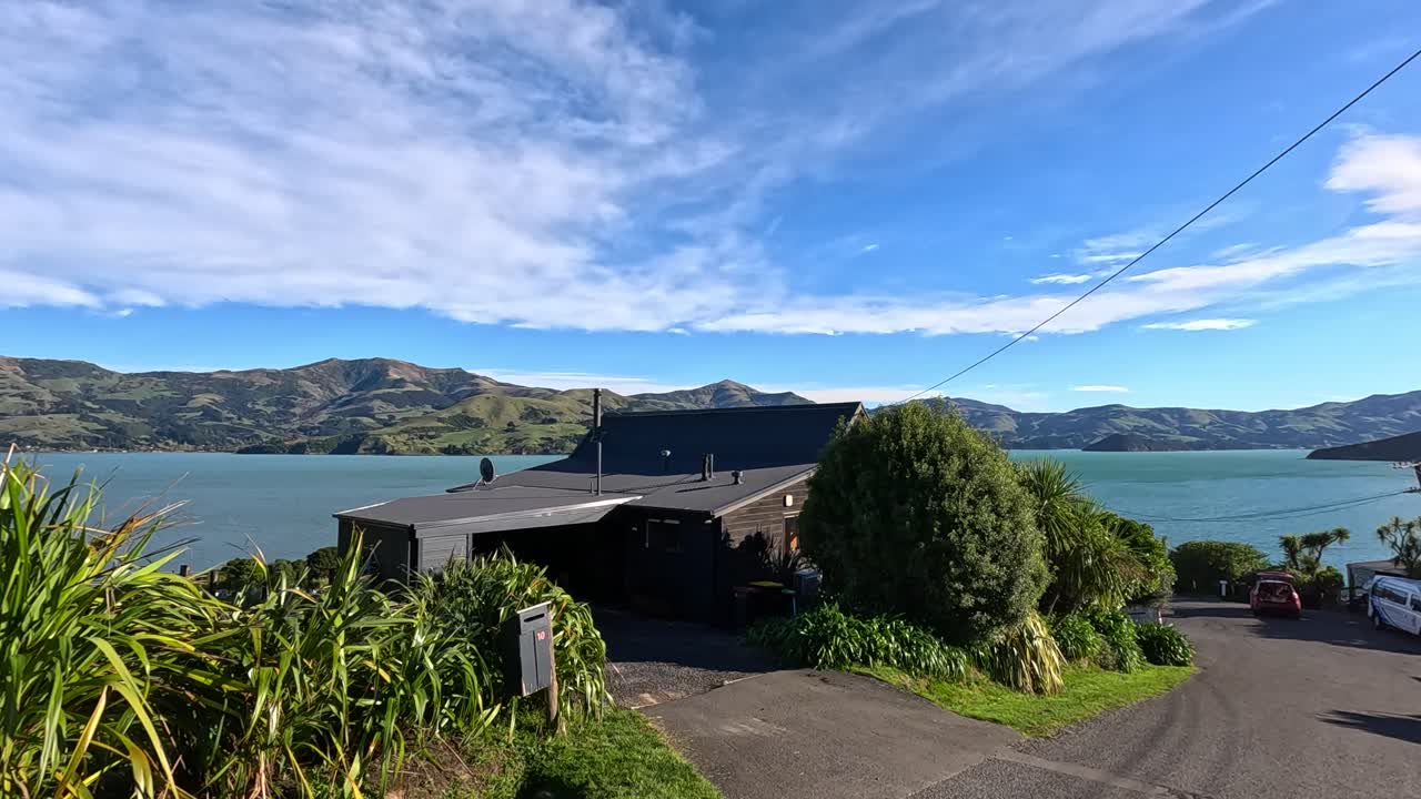 Aerial view of Akaroa's coastal road, showcasing vibrant greenery, blue skies, and serene waters under bright sunlight