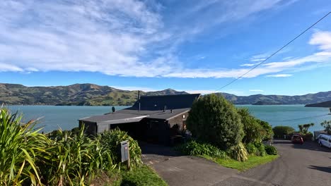aerial view of akaroa's coastal road, showcasing vibrant greenery, blue skies, and serene waters under bright sunlight