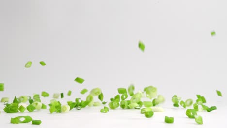 diced and chopped green onion pieces falling and bouncing onto white table top in slow motion