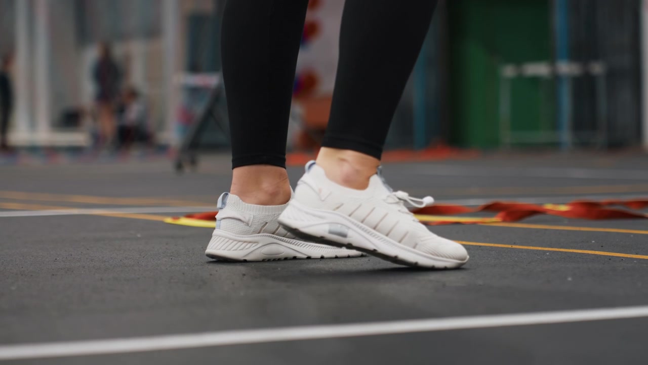 Juego de pies en una cancha de bádminton, mostrando zapatillas blancas y leggings negros, ejecutando pasos precisos durante un ejercicio de entrenamiento individual en una pista cubierta, enfocado en la mejora del ritmo, el equilibrio y la agilidad.