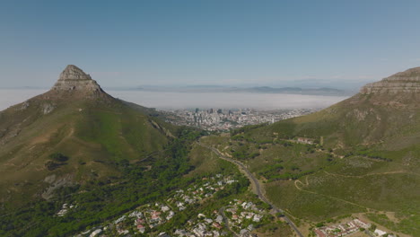 Vista-Aérea-Del-Paso-De-Montaña-Entre-La-Cabeza-De-Leones-Y-La-Montaña-De-La-Mesa.-Edificio-Céntrico-De-Gran-Altura-En-La-Distancia.-Ciudad-Del-Cabo,-Sudáfrica