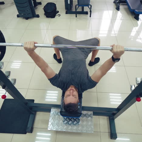handsome man is working out chest with barbell in a modern gym