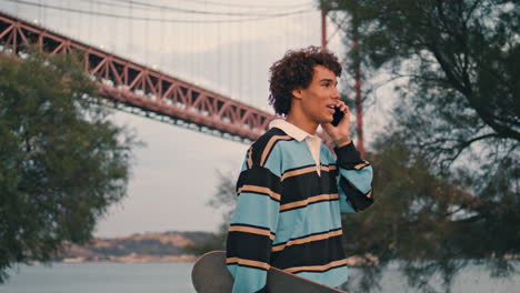 friendly teenager speaking smartphone at embankment. guy talking mobile vertical