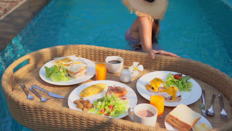 Woman-with-hat-in-hotel-swimming-pool-with-floating-tray-of-food