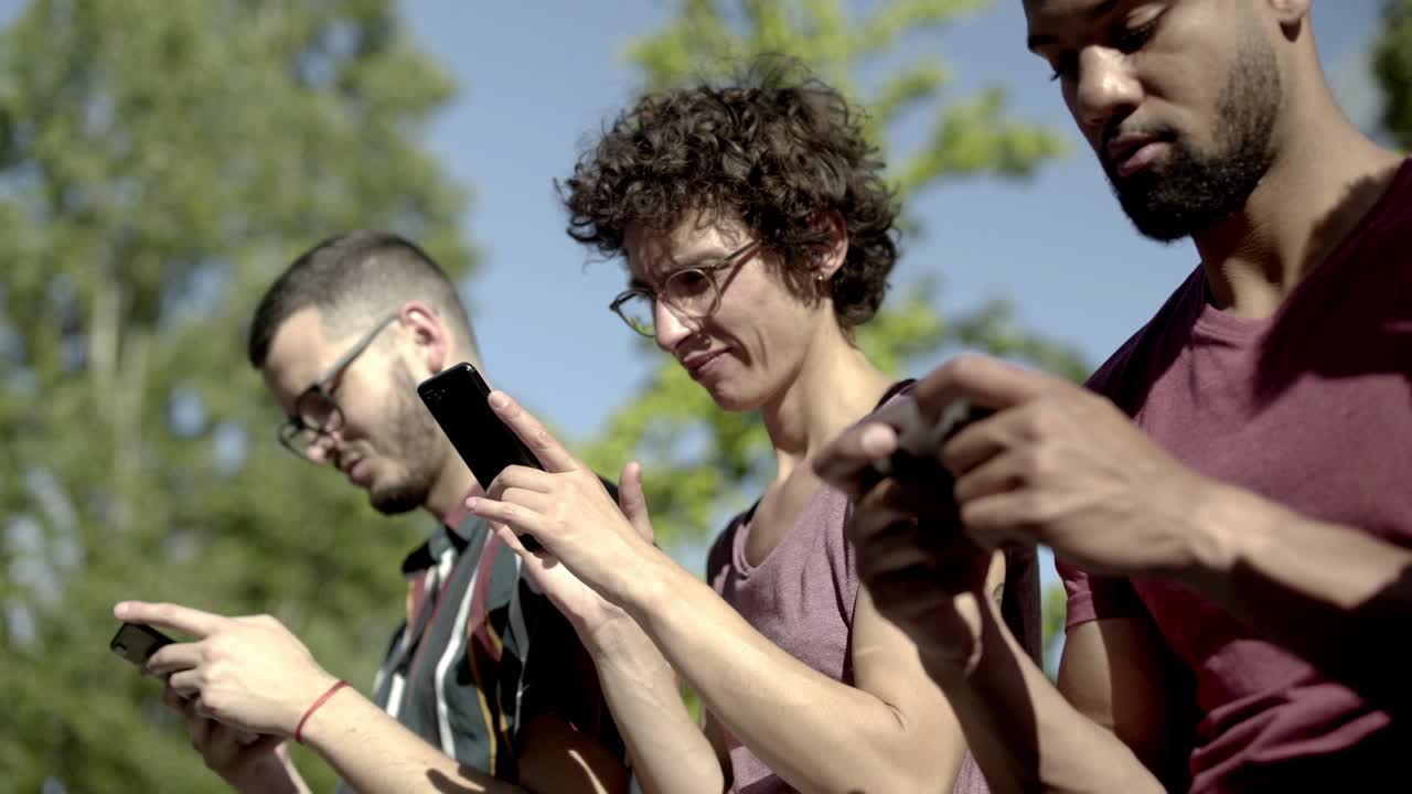 amigos concentrados sentados en el parque y usando teléfonos inteligentes.