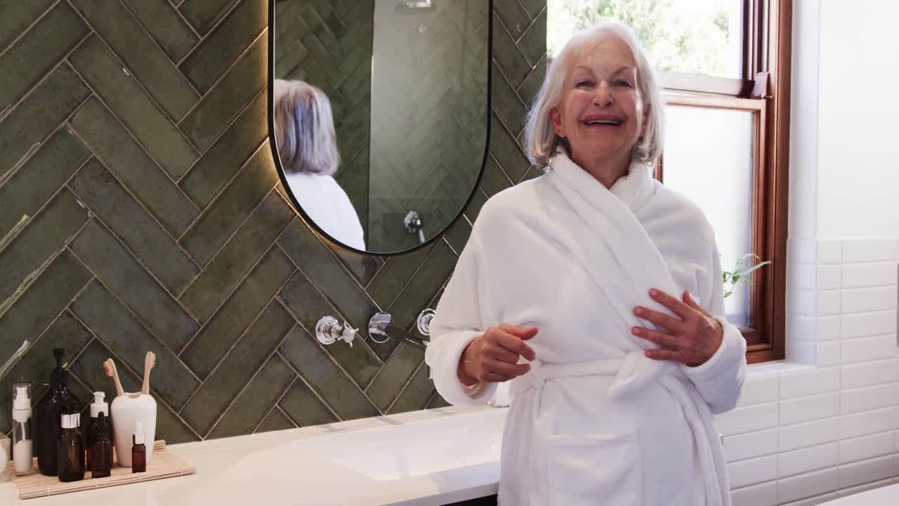 In bathroom, senior woman in bathrobe smiling joyfully, feeling relaxed, at home