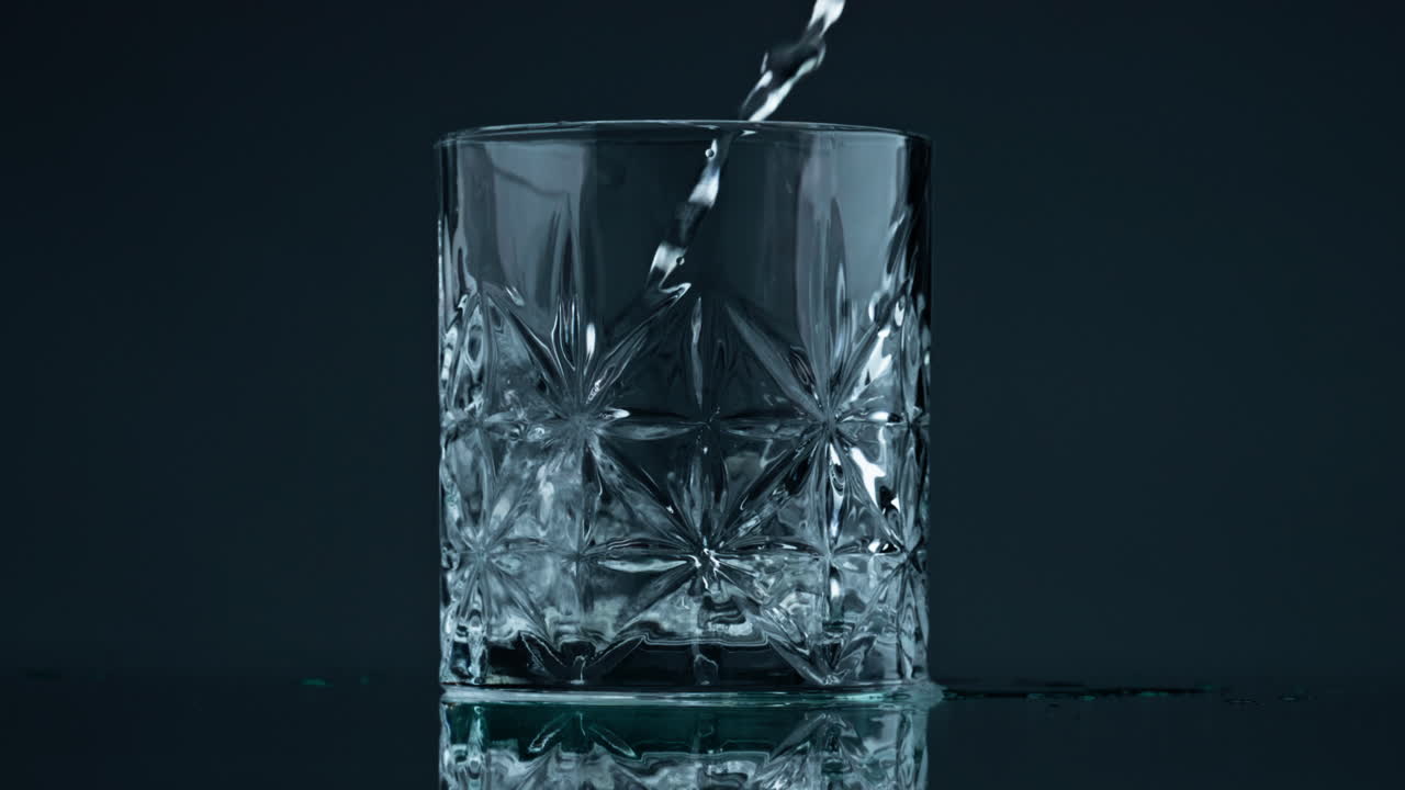 Pouring water crystal glass at dark background closeup. Liquid stream falling