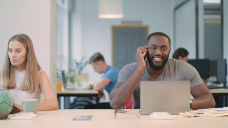 Smiling-guy-talking-mobile-phone-at-coworking-space.-Man-chatting-with-phone