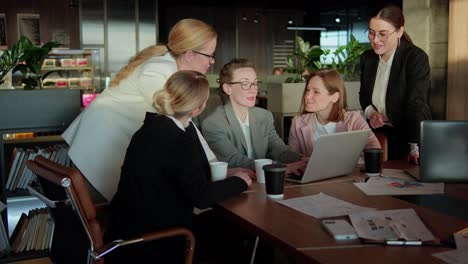 confident group business woman in business clothes sitting at a table in the office in front of a laptop and communicating about solving their problem and current ideas about work in the office