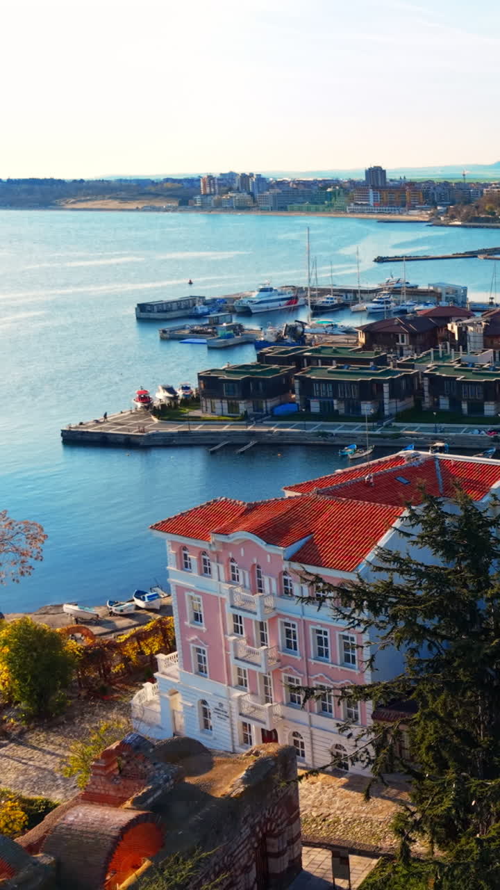 Edificio classico rosa con appartamenti moderni e un porto turistico per yacht sullo sfondo. Appartamenti di lusso e marina sul Mar Nero. Video verticale