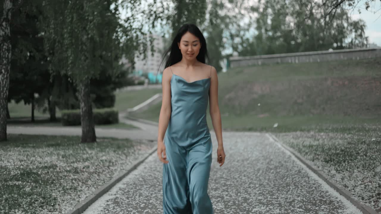 Woman in a Blue Satin Dress Walking in a Park