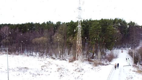 high voltage electric pole standing near forest during heavy snowfall, aerial descend view