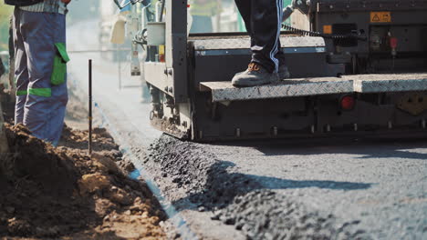Asphalt paver machine laying hot asphalt to the road and workers control. Spillage of asphalt on the highway. Fresh asphalt resurfacing the street. New service of technology asphalting.