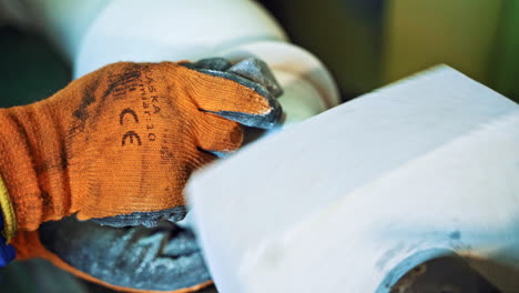 hand of a worker in protective glove is holding stone at the electric machine. man is polishing stone on the circular machine at factory. close-up.