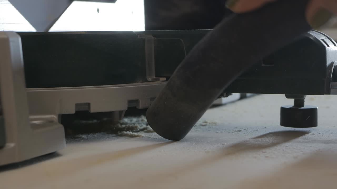 일하는 목수 여성은 작업장을 조직합니다. 그녀는 공업용 진공청소기로 기계 주변과 기계 의 먼지를 청소합니다.