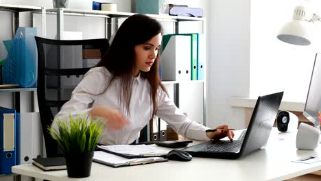 mujer de negocios trabajando en una computadora portátil y escribiendo en papel en una oficina moderna