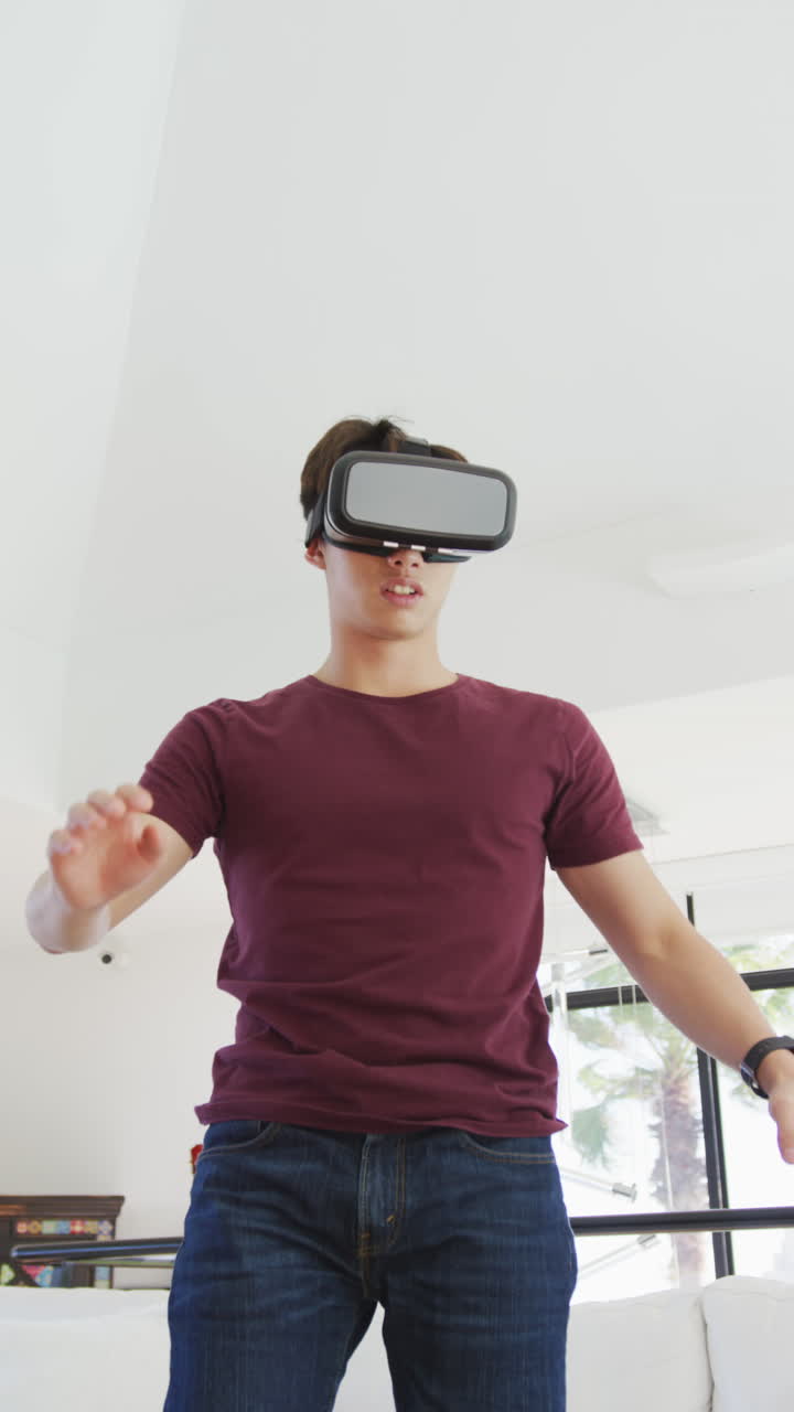 Video verticale di un ragazzo adolescente asiatico che usa un visore VR nel soggiorno