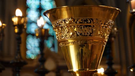 ornate golden chalice standing on a pedestal in a church, with stained glass windows in the background