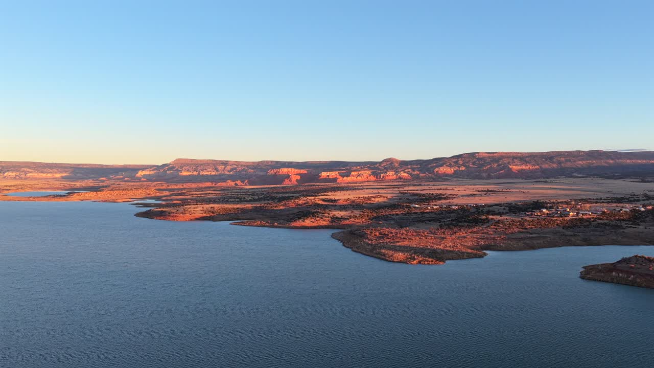 Drone footage moves smoothly along the dramatic red rock cliffs and clear blue water of Abiquiu Lake, New Mexico. This striking high desert landscape is evocative of the Southwest mesas