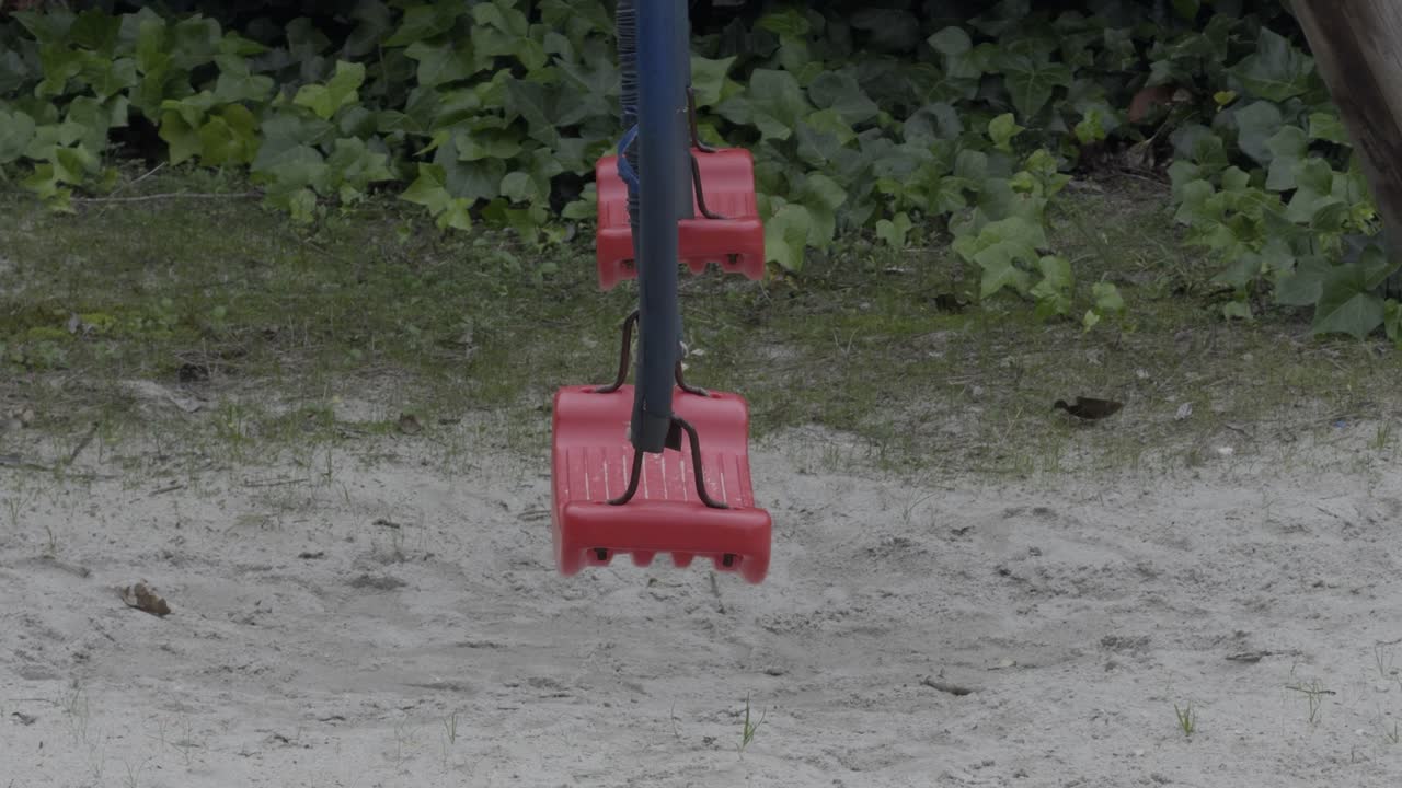 columpios rojos con cadenas negras de pie en el parque de arena con algunas plantas