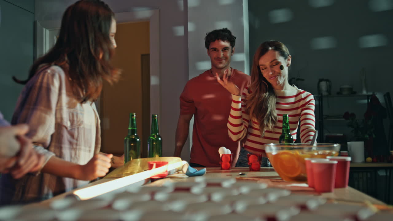 Estudiantes jugando beer pong en una fiesta en casa con luces intermitentes. Gente socializando