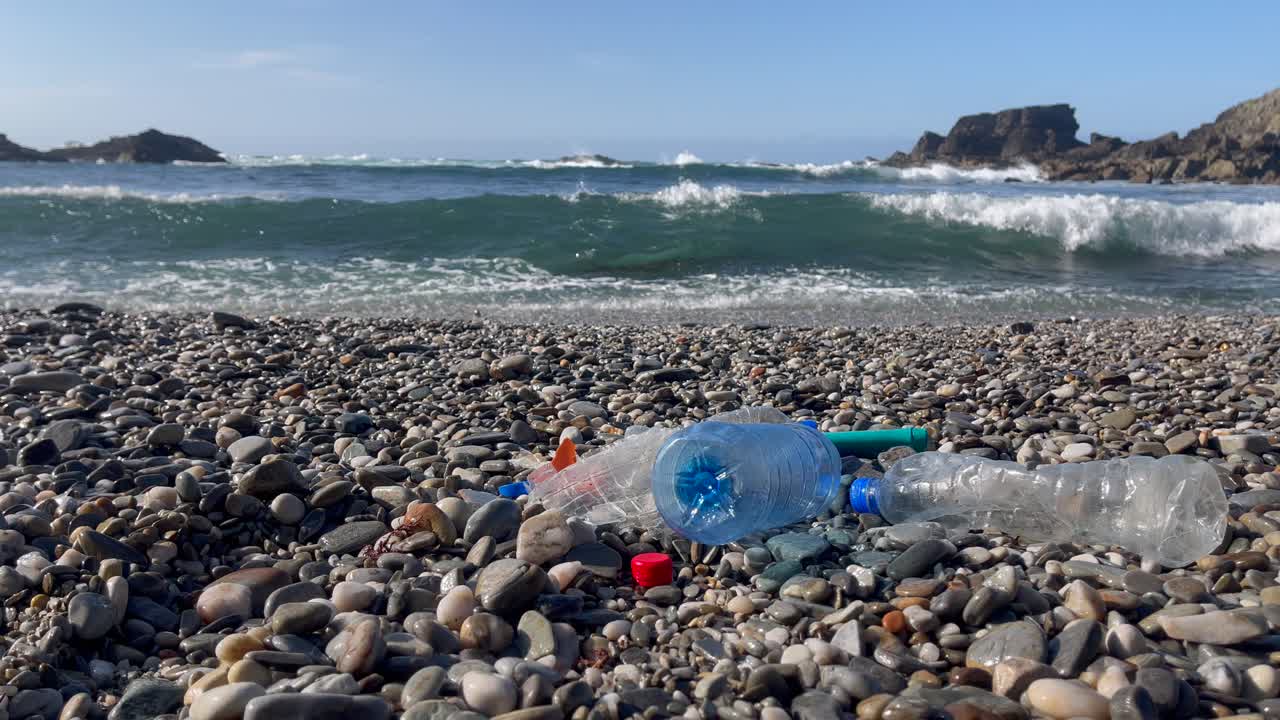 플라스틱 쓰레기와 병 쓰레기 바위 해변 배경에는 바다 파도가 있습니다.
