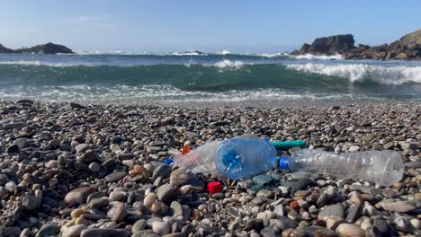 plastic waste and bottles litter rocky beach with ocean waves in background