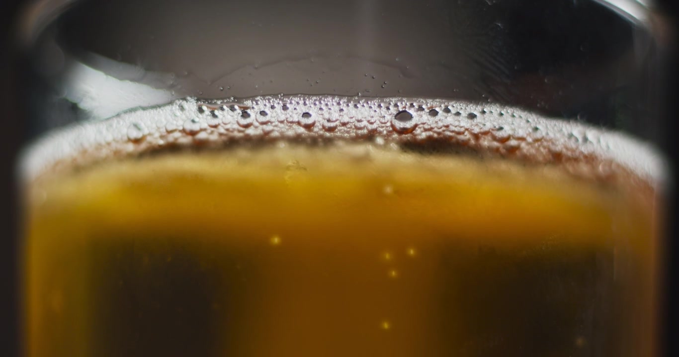 Primo piano macro di un bicchiere da pinta mentre la telecamera si inclina verso l'alto e segue le bollicine che salgono al rallentatore con una testa di schiuma