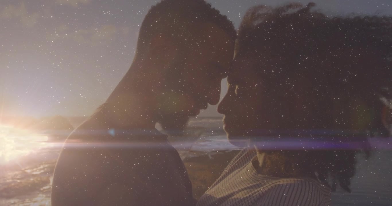 Homem se aproximando e mulher respondendo na costa, com um toque de romance e um brilho de lente que molda os contornos.