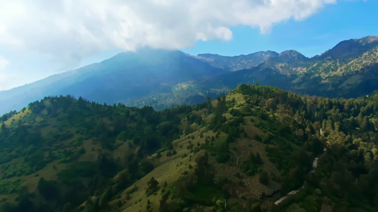 Forested mountain slopes with rugged ridges leading to Nevado de Colima peak partly covered by clouds