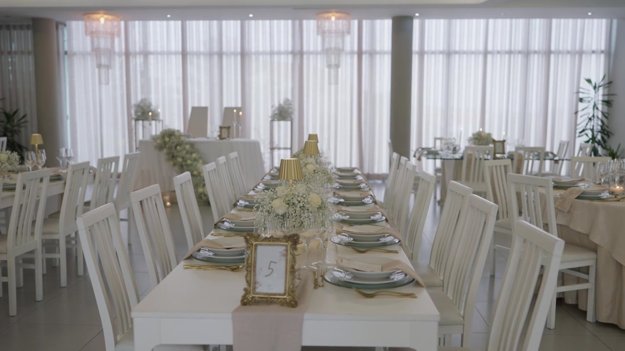 Elegante salón de banquetes para recepción de bodas con mesas largas puestas, sillas blancas y decoración floral
