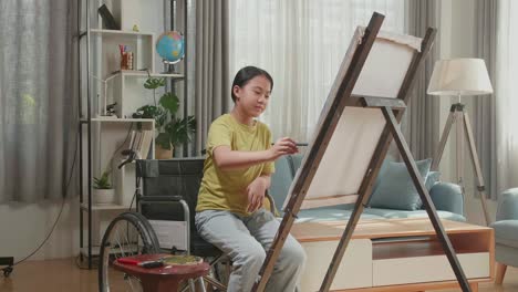 asian artist girl in wheelchair holding paintbrush mixed colour and thinking before painting on the canvas