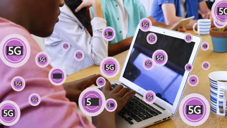 Animation-Von-5G-Text-Mit-Symbolen-über-Einem-Afroamerikanischen-Mann,-Der-Im-Büro-Am-Laptop-Arbeitet