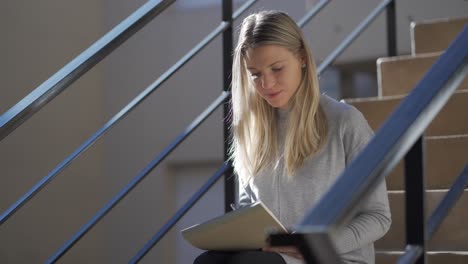 eine fröhliche blonde frau, die auf der treppe sitzt und auf ein notizbuch schreibt