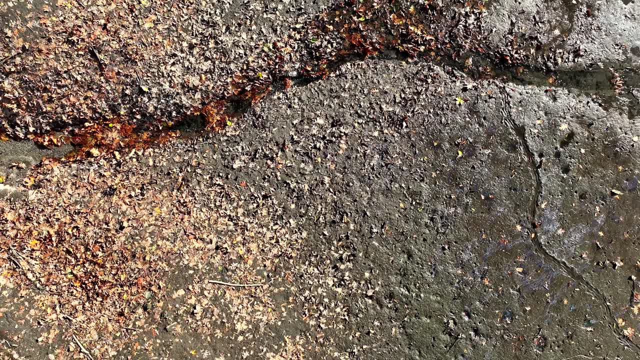 Top down tracking along trickling water through pipe emptying into muddy riverbed, aerial