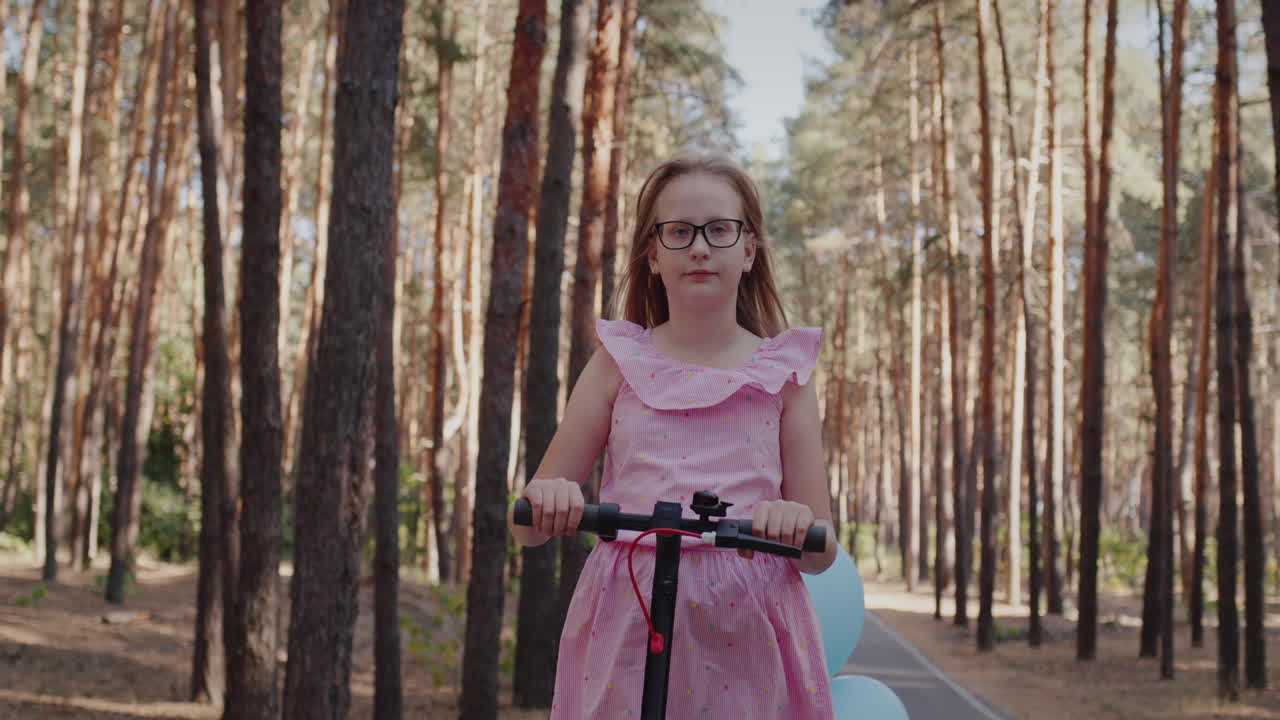 분홍색 드레스를 입은 소녀는 공원에서 스쿠터를 탄다