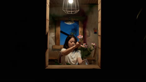 outside view into a home where a young woman is cutting flowers to fit into a vase