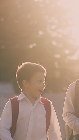 young happy schoolboys in uniform walk along road after passing exam against green trees hiding sun slow motion