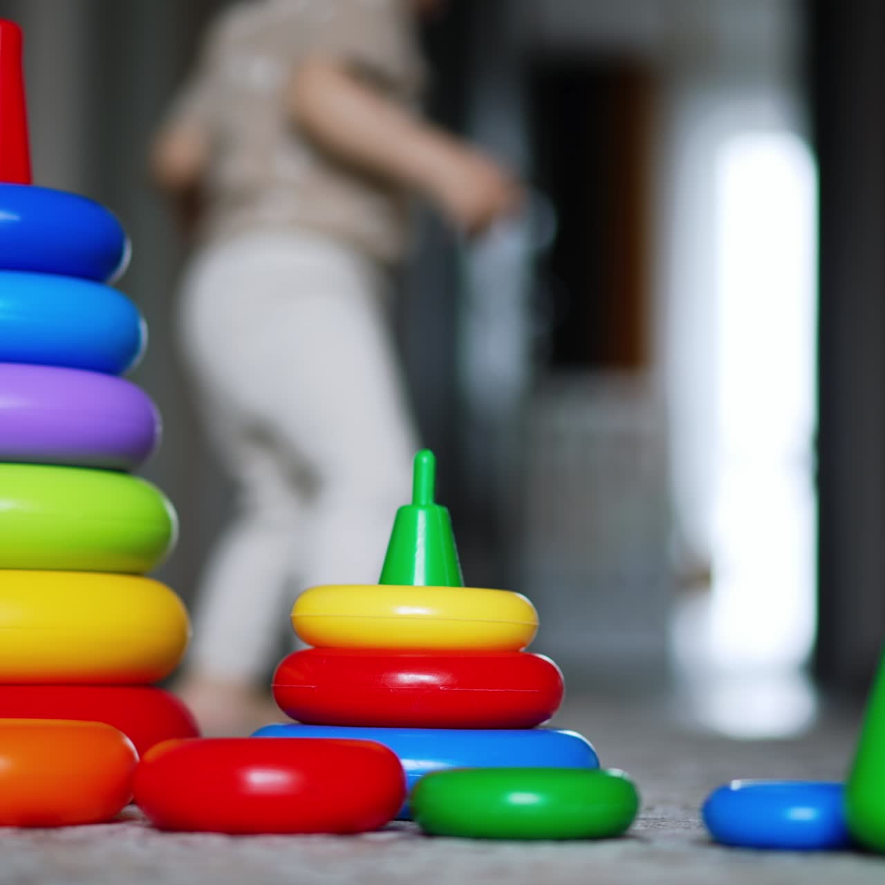Smaller and bigger pyramid on the floor. Kid comes up to toys but then walks away. Blurred backdrop