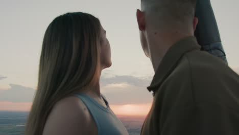 close up of couple enjoying sunset gaze as distant red paraglider drifts across pastel sky above sprawling farmland under soft clouds creating serene romantic aerial adventure moment